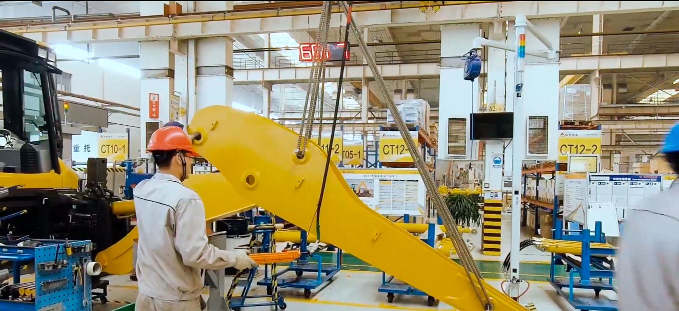 Um homem de uniforme bege e capacete laranja operando uma máquina na fábrica da SDLG