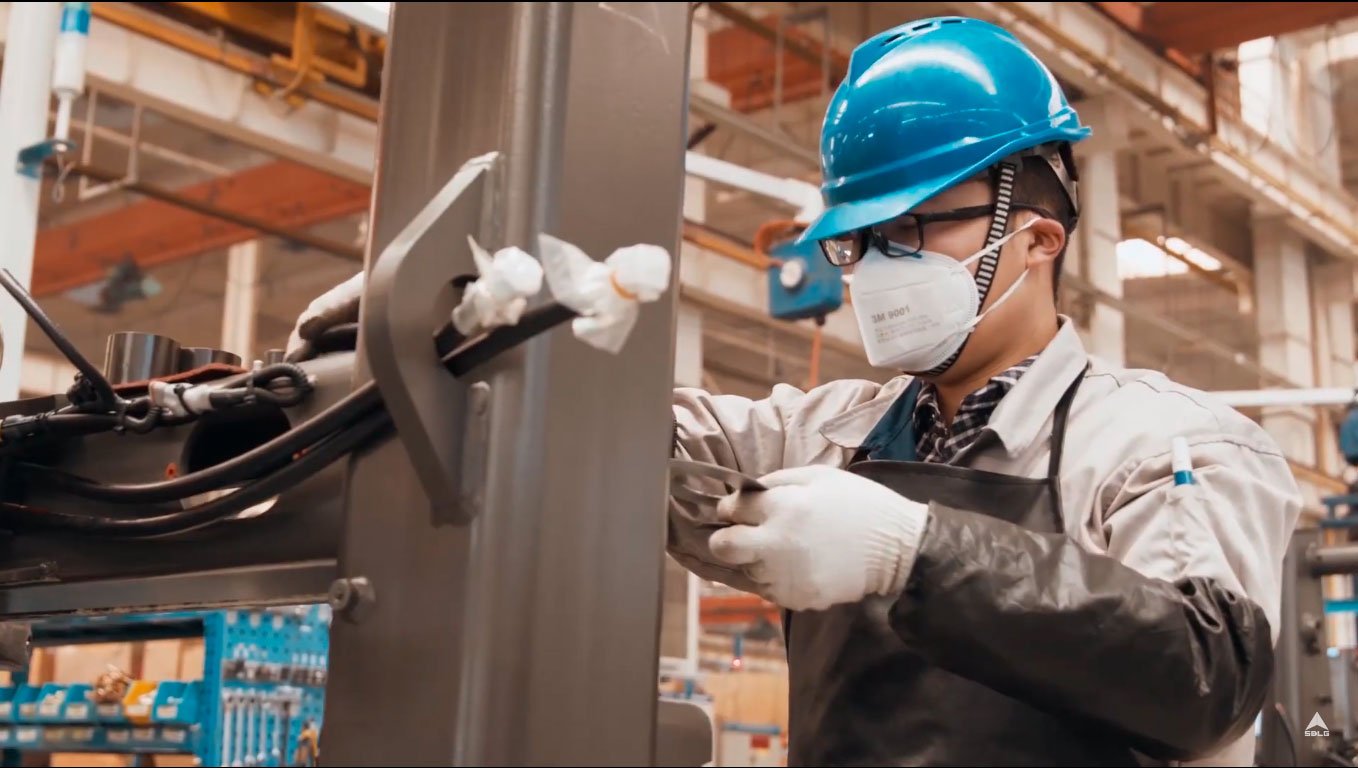 Um homem de uniforme bege e capacete azul fazendo ajustes em uma máquina em construção