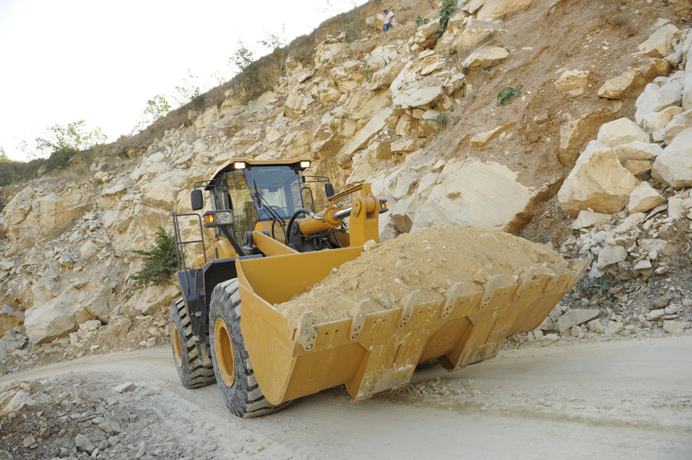 Cargadora de ruedas sdlg amarillo, transportando arena en un camino sin pavimentar, algunas rocas en el fondo.