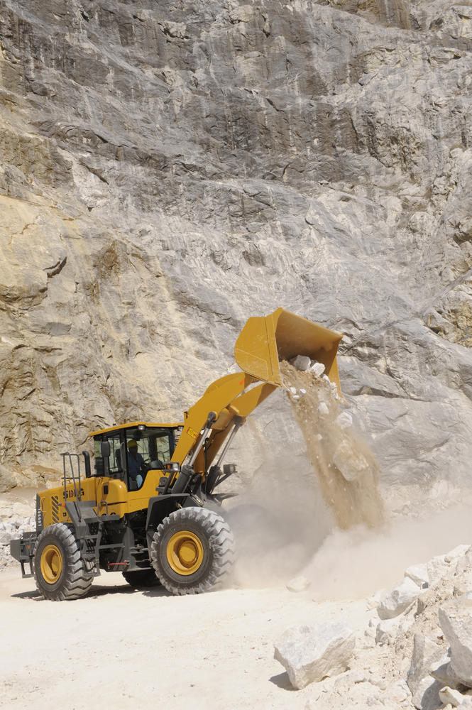 Cargadora de ruedas amarillo SDLG, tirando arena, en el fondo un muro de piedra