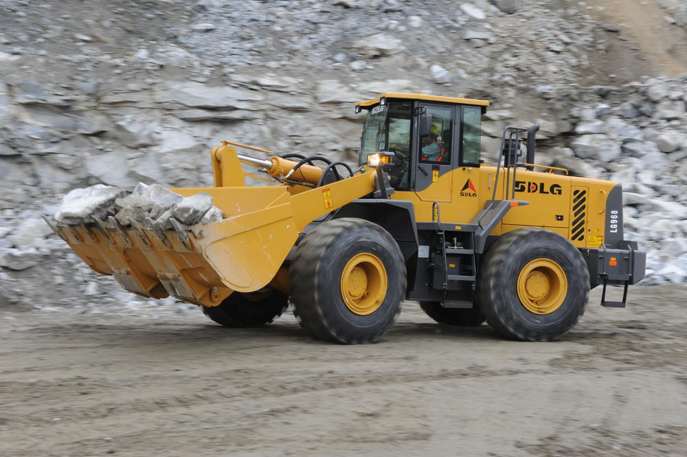 Cargadora de ruedas SDLG LG968, transportando piedra en un camino sin pavimentar, algunas rocas en el fondo