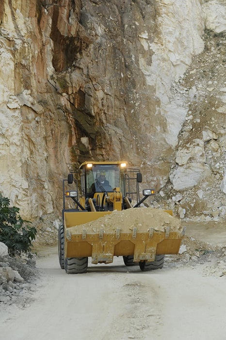 Cargadora de ruedas sdlg amarillo, transportando arena en un camino sin pavimentar, con una pared de roca al fondo.