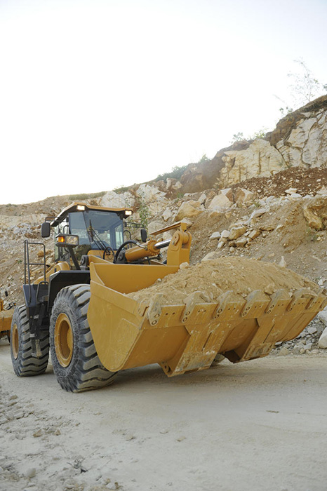 Cargadora de ruedas sdlg amarillo, transportando arena en un camino sin pavimentar, en el fondo algunas rocas y el cielo nublado.