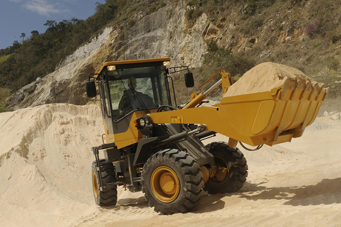 Cargadora SDLG LG918, llena de arena, con el brazo de la máquina a media altura. Al fondo, un montón de arena y vegetación sobre un cerro.