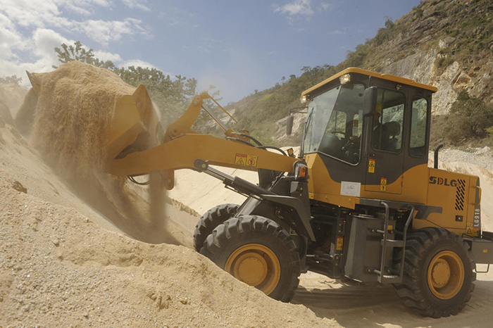 Cargador SDLG LG918, arena desbordante, con brazo de máquina a media altura. Al fondo, vegetación sobre un cerro.