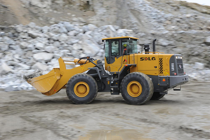 Cargadora de ruedas SDLG LG968, transportando piedra en un camino sin pavimentar, algunas rocas en el fondo