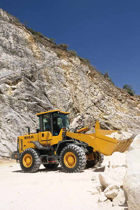 Cargadora SDLG LG936L, transportando piedra, colina con rocas al fondo.