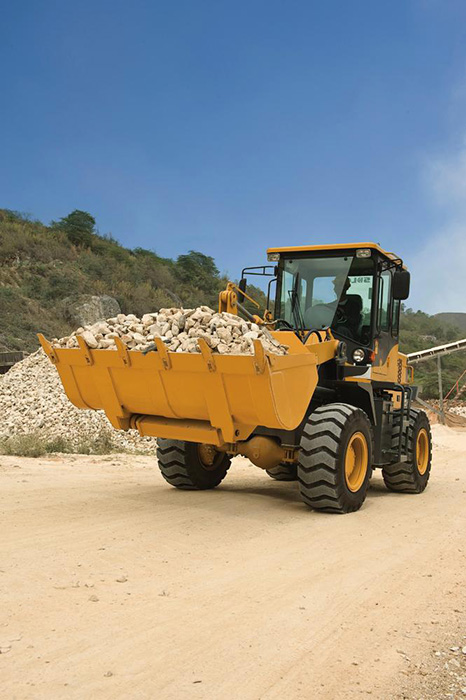 Cargadora SDLG, transportando piedra, vegetación al fondo.