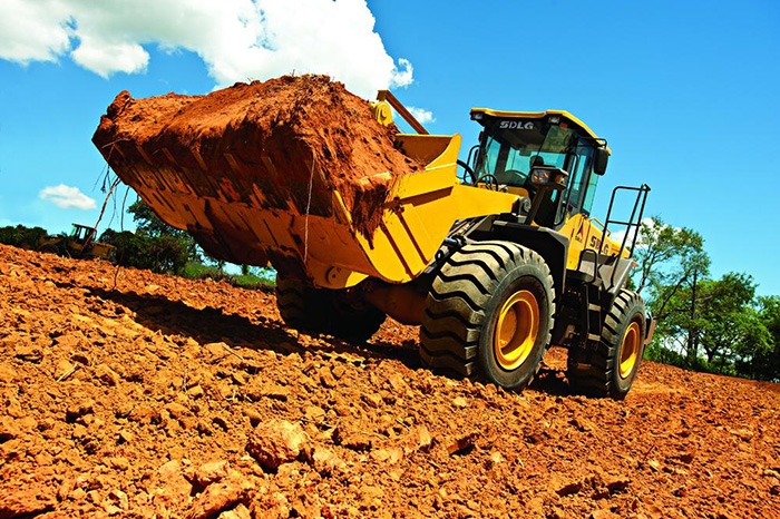 Cargadora de ruedas SDLG LG958L, cargada con tierra sobre un piso de tierra y un cielo azul