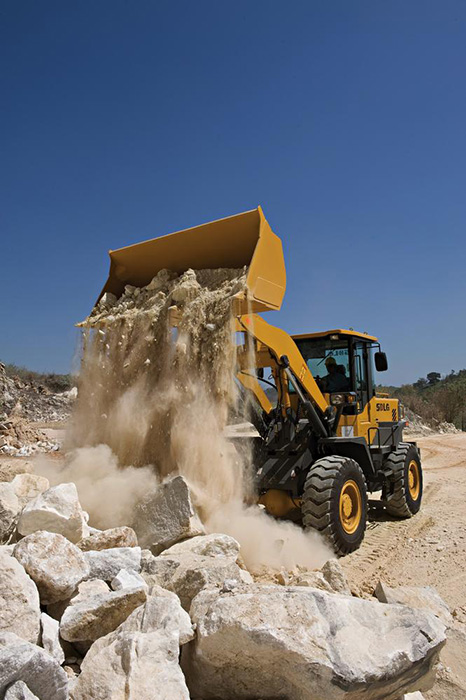 Cargadora SDLG, en funcionamiento descargando piedras al fondo unos arboles