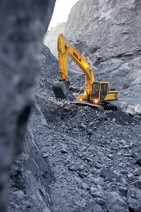 Excavadora SDLG, excavando grava, entre dos colinas rocosas.