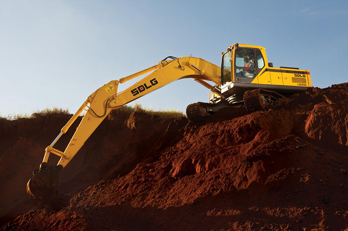 Excavadora SDLG, la máquina está encima de un banco de tierra, recogiendo tierra de la parte inferior.