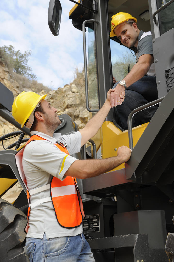 Un trabajador dentro del cargador SDLG le da mano a otro trabajador que está parado a un lado
