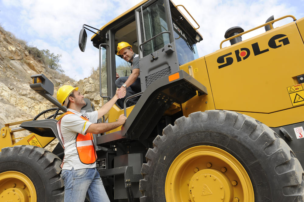 Un trabajador dentro del cargador SDLG le da mano a otro trabajador que está parado a un lado