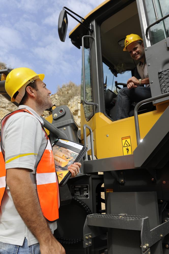 Un trabajador está dentro del cargador hablando con outro trabajador que está parado a un lado , al fondo un muro de piedra 