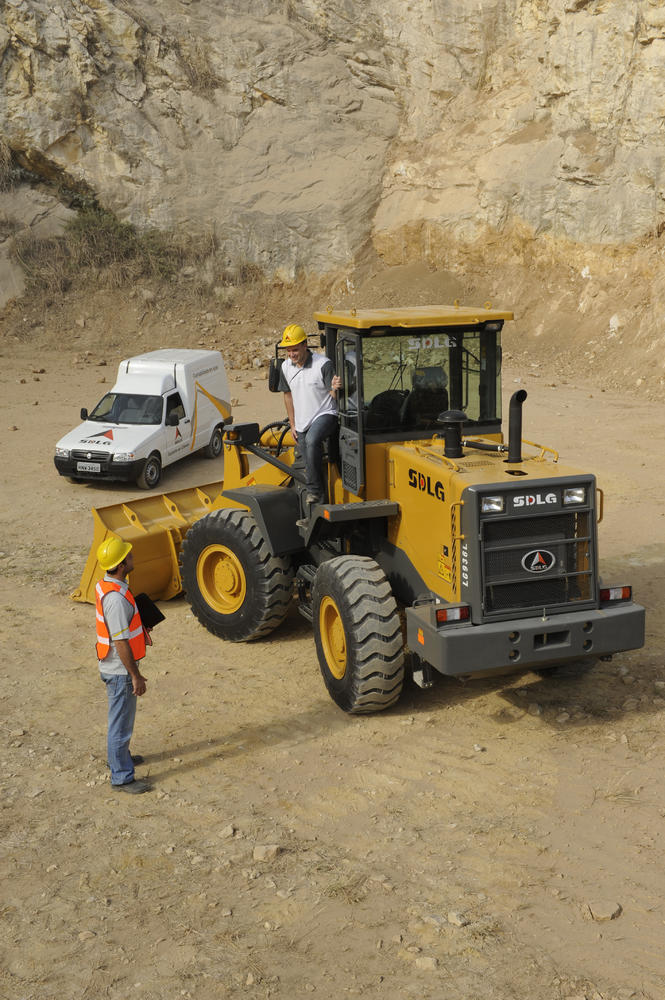 Dos trabajadores hablando junto a la cargadora SDLG, al fondo un coche blanco y um muro de piedra
