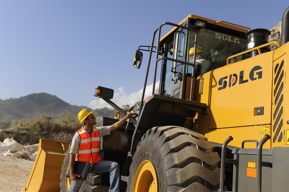 Dos trabajadores conversando, uno dentro de la cabina de la cargadora SDLG LG958L y el otro al costado, al fondo montanãs 