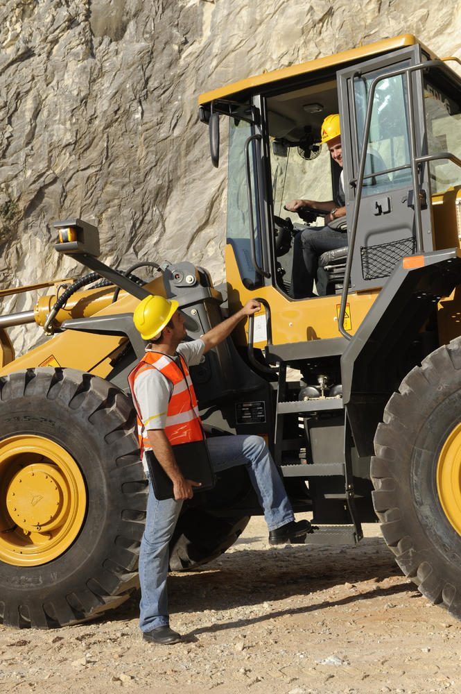 Dos trabajadores conversando, uno dentro de la cabina de la cargadora SDLG LG958L y el otro al costado, al fondo un muro de piedra 