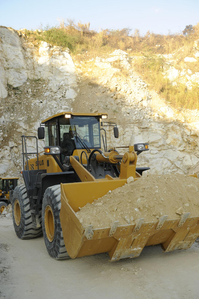Cargadora SDLG que transporta tierra y piedra em el fondo de una montanã de piedra