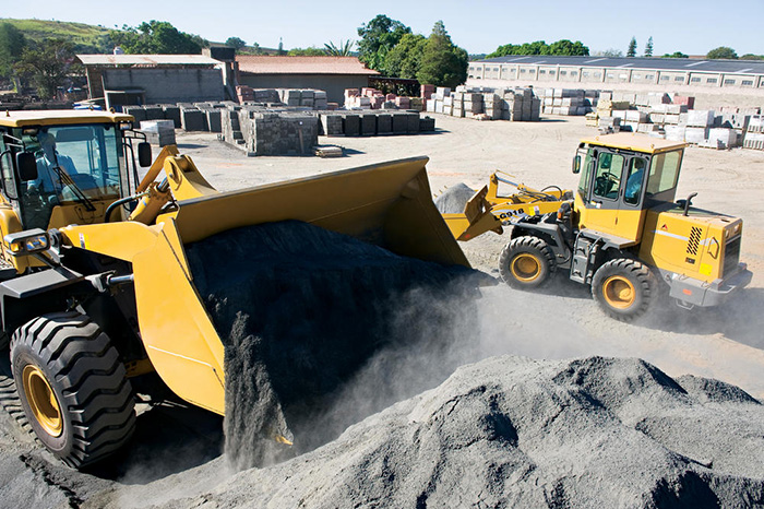 Cargadora de ruedas SDLG descargando arena en un almacén de materiales de construcción.