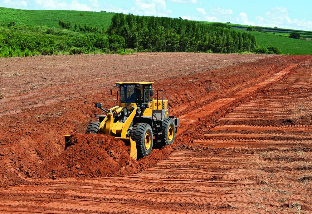 Cargador SDLG moviendo la tierra en una plantación, en el fondo una gran zona verde con algunos árboles