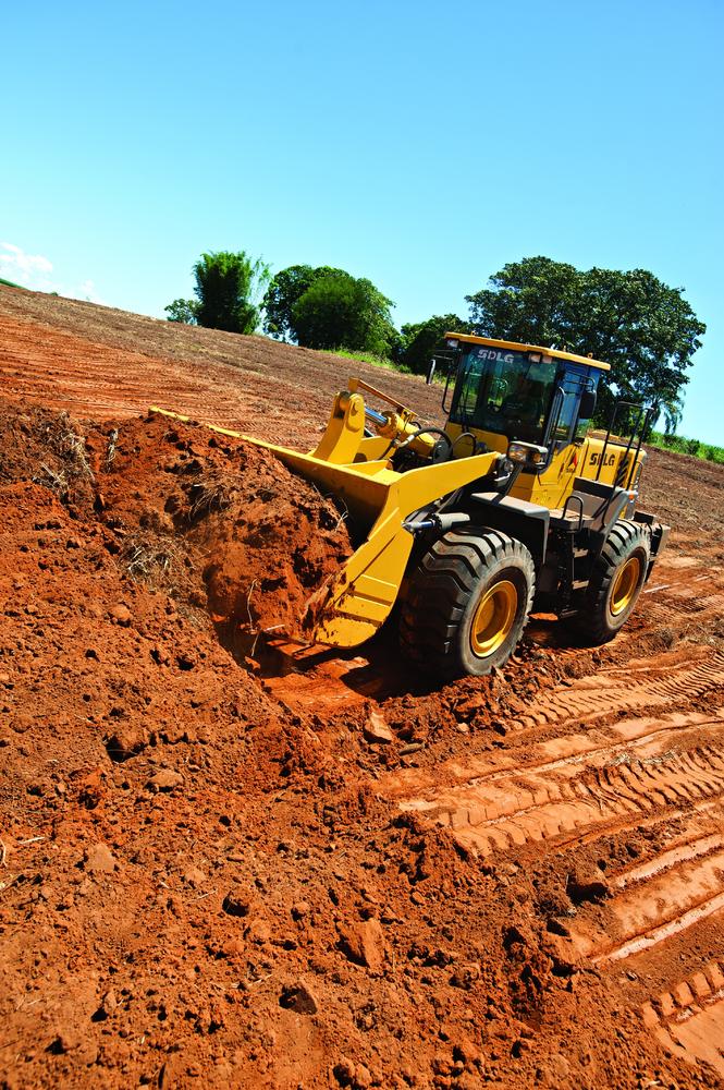 Cargadora de ruedas SDLG moviendo tierra en un área de plantación, algunos árboles en el fondo