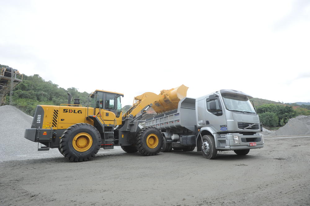 Cargadora de ruedas SDLG LG968 descargando rocas en un camión gris, con árboles y piedras en el fondo