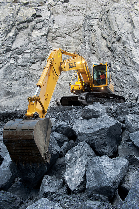 Excavadora SDLG, excavando en una cantera, con el brazo de la máquina bien extendido, al fondo una pared de rocas.