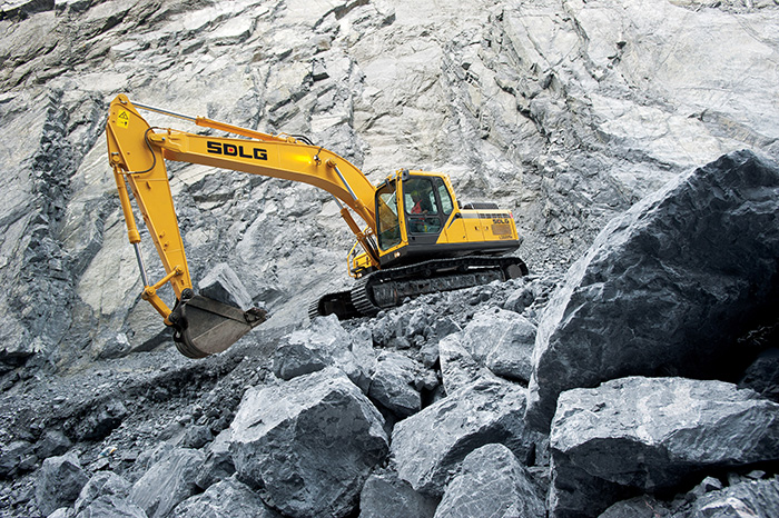 Excavadora SDLG, excavando en una cantera, al fondo una pared de rocas.