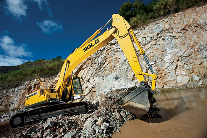 Excavadora SDLG, quitando tierra del suelo, al fondo una pared de rocas.
