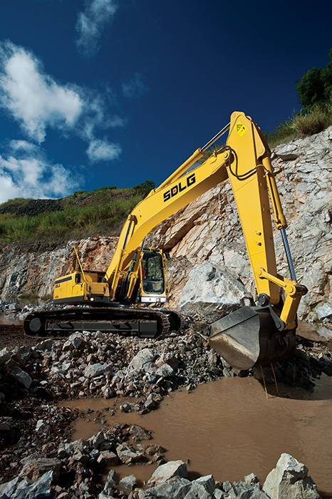 Excavadora SDLG, quitando tierra del suelo, al fondo una pared de rocas.