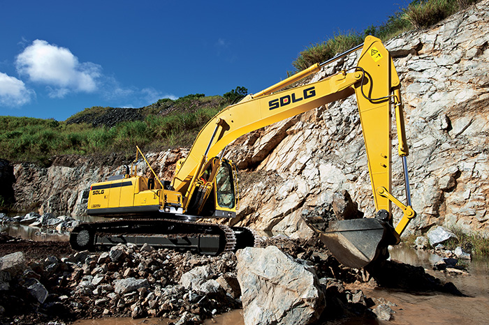 Excavadora SDLG, quitando tierra del suelo, al fondo una pared de rocas.