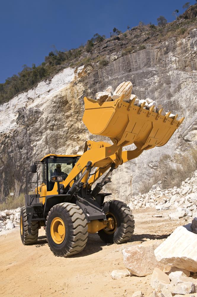 Cargador SDLG en funcionamiento transportando piedras en el fondo de un muro de piedra