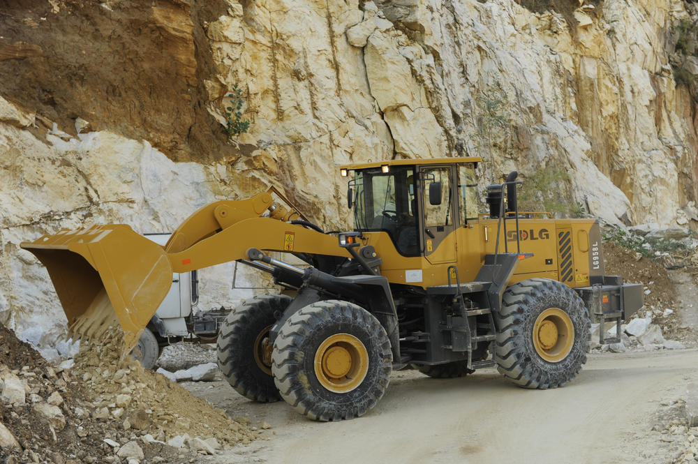 Cargadora de ruedas LG958L SDLG descargando piedras y tierra, con un muro de piedra al fondo