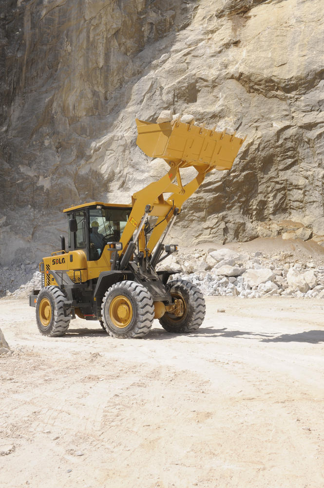 Cargadora de ruedas SDLG transportando piedras, un muro de piedra al fondo