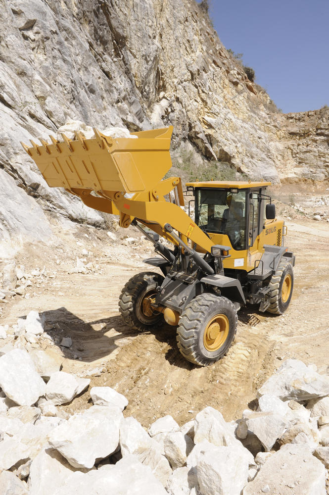 Cargadora de ruedas SDLG, acarreando piedras, brazo de la máquina levantado.