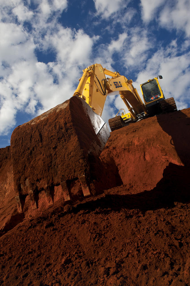 Excavadora SDLG, recogiendo tierra, en el fondo un cielo azul.