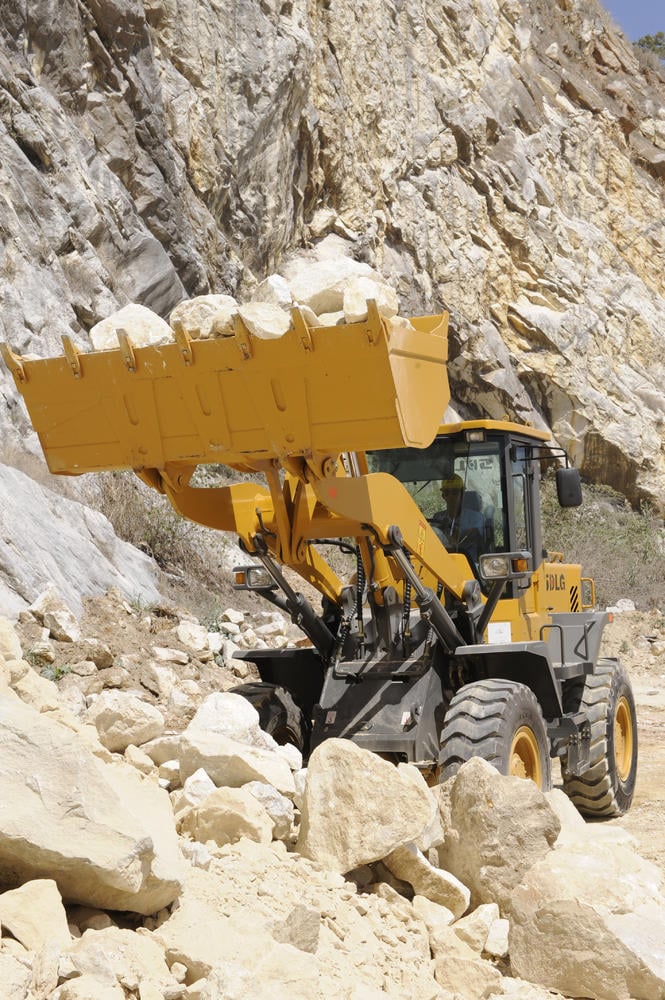 Cargadora SDLG, transportando piedras, con el brazo de la máquina levantado, al fondo una pared de rocas.