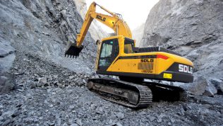 Excavadora SDLG, excavando en un terreno irregular, con una pared de rocas al fondo.