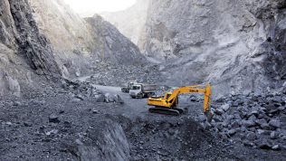 Excavadora SDLG, excavando en un terreno irregular, con una pared de rocas al fondo.