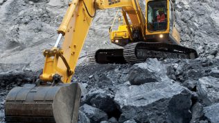 Excavadora SDLG, excavando en una cantera, con el brazo de la máquina bien extendido, al fondo una pared de rocas.