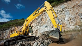 Excavadora SDLG, quitando tierra del suelo, al fondo una pared de rocas.