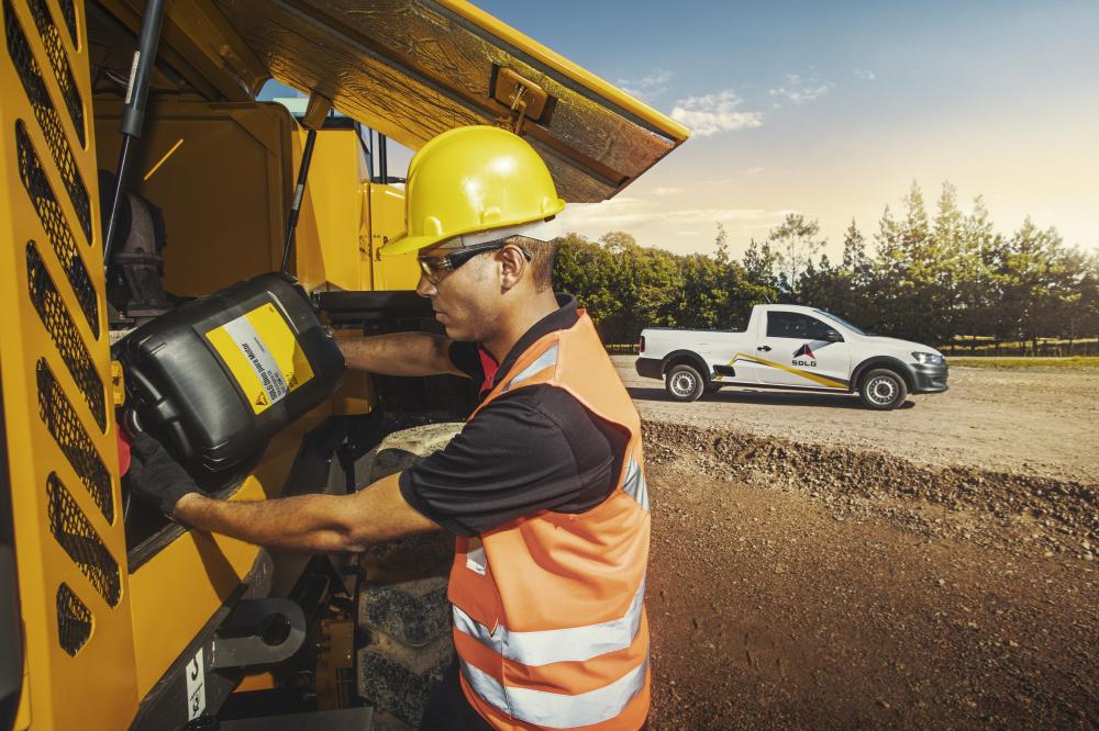 Um homem de colete laranja e capacete amarelo colocando óleo em uma máquina SDLG