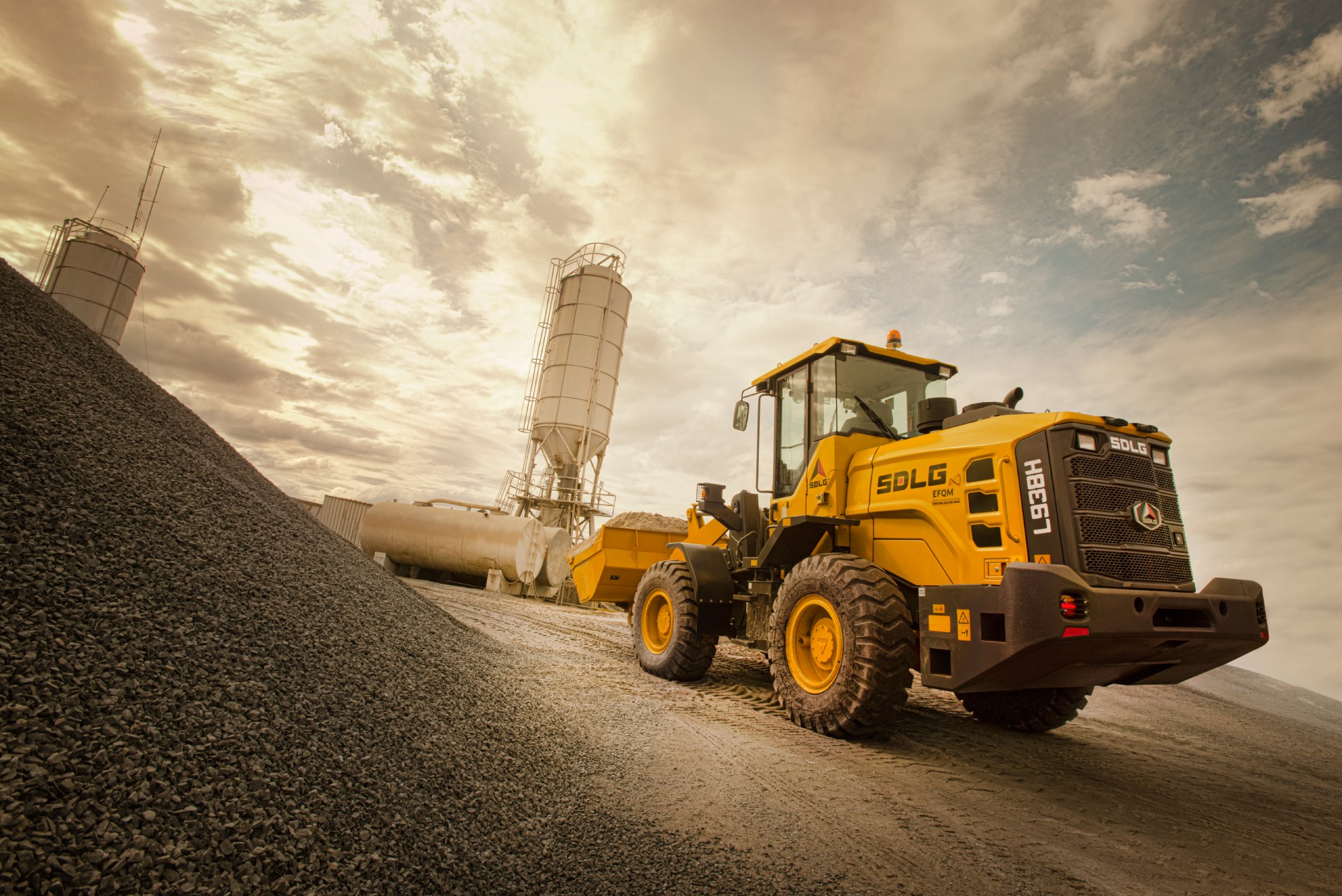 Cargador SDLG modelo L938H, lleno de piedra, junto a una industria.