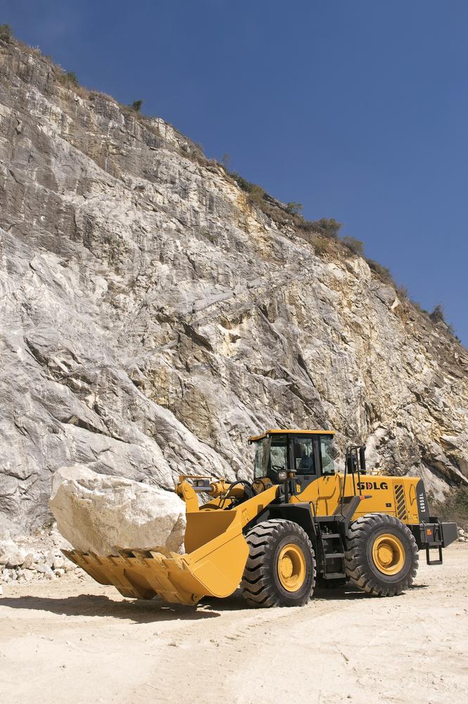 Cargador SDLG, llevando una roca, al fondo una pared de rocas.