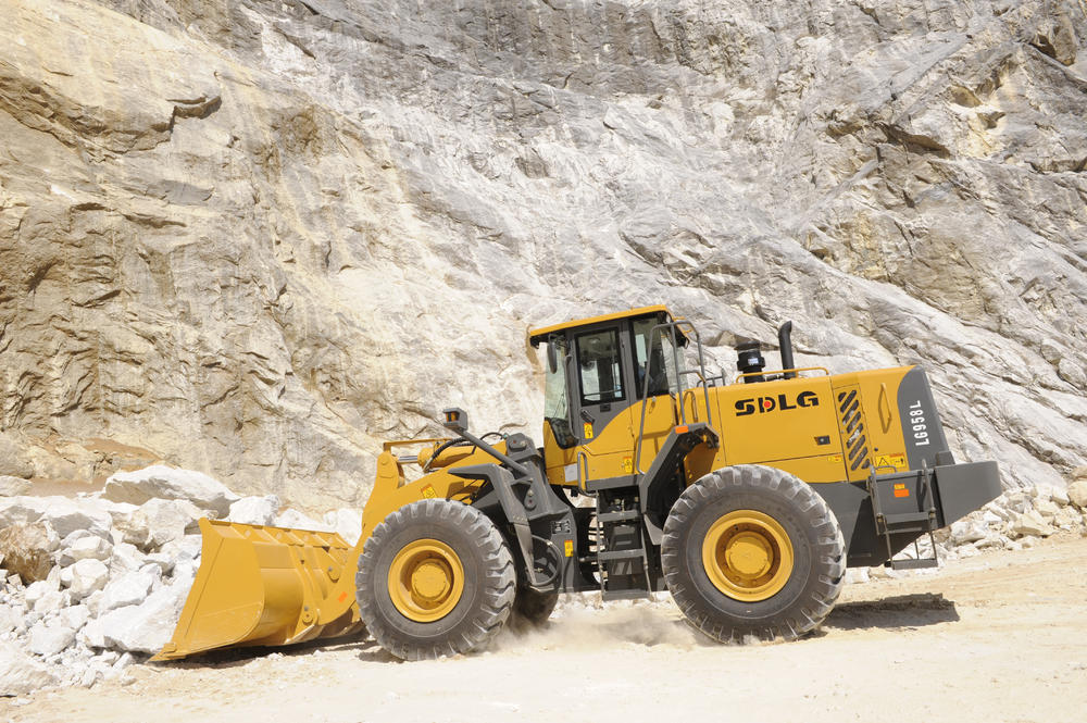 Cargadora SDLG modelo LG958L, cargando rocas, al fondo una pared de rocas.