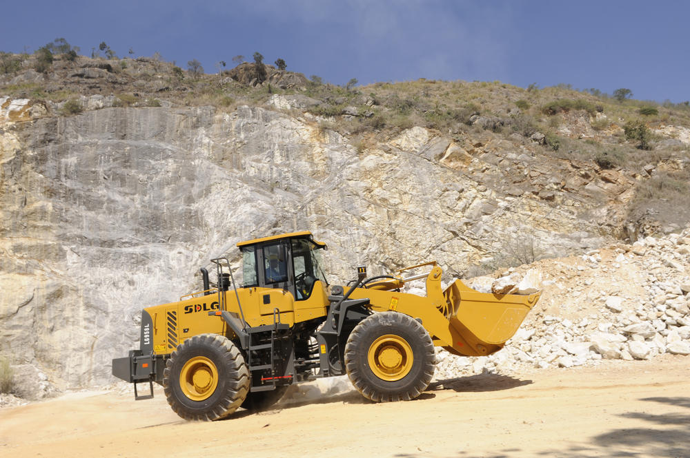 Cargadora SDLG modelo LG958L, cargando rocas, al fondo una pared de rocas.