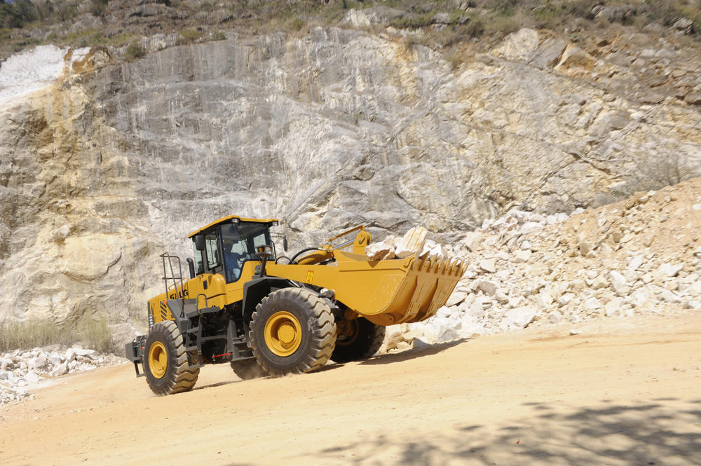 Cargadora SDLG modelo LG958L, cargando rocas, al fondo una pared de rocas.