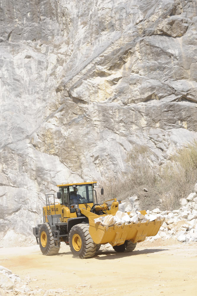 Cargadora SDLG modelo LG958L, cargando rocas, al fondo una pared de rocas.