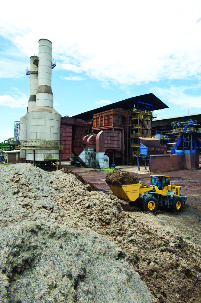 Cargador SDLG, lleno de tierra, al fondo una industria.